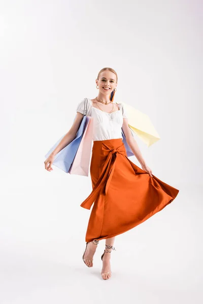 Full length view of elegant woman walking with shopping bags on white — Stock Photo