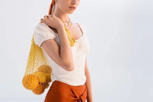 Vista ritagliata di donna rustica in posa con agrumi in sacchetto di stringa giallo isolato su bianco — Foto stock