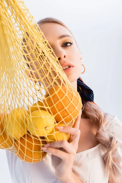 Mulher loira rústica posando com frutas cítricas em saco de corda amarela isolado no branco — Fotografia de Stock