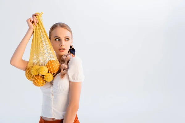 Donna bionda rustica in posa con agrumi in sacchetto di stringa giallo isolato su bianco — Foto stock