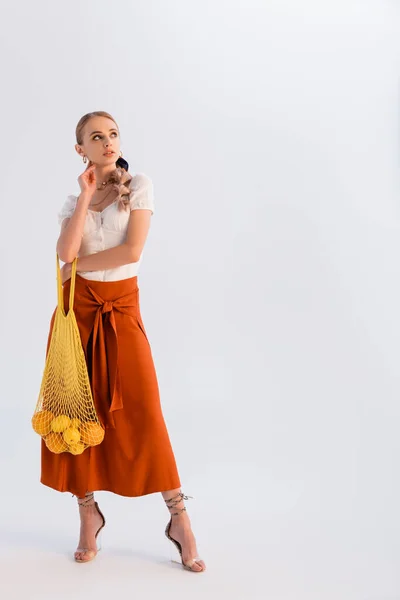 Sonhador rústico mulher loira posando com frutas cítricas em saco de cordas amarelo isolado no branco — Fotografia de Stock