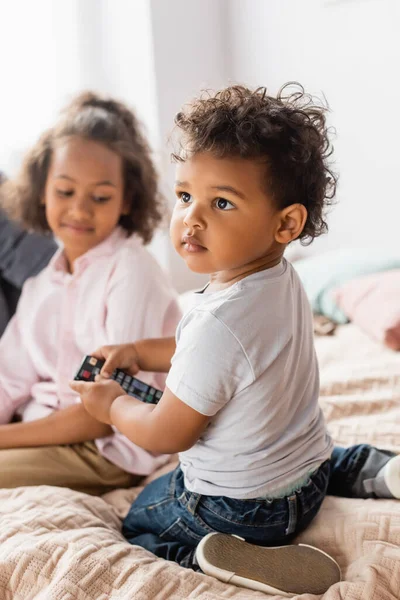 Selektiver Fokus eines afrikanisch-amerikanischen Jungen im weißen T-Shirt, der eine Fernbedienung in der Nähe der Schwester hält — Stockfoto