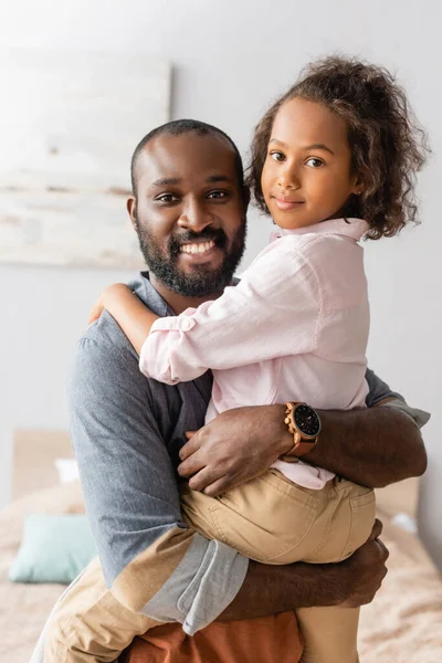 Bearded african american man holding daughter on hands while looking at camera — Stock Photo