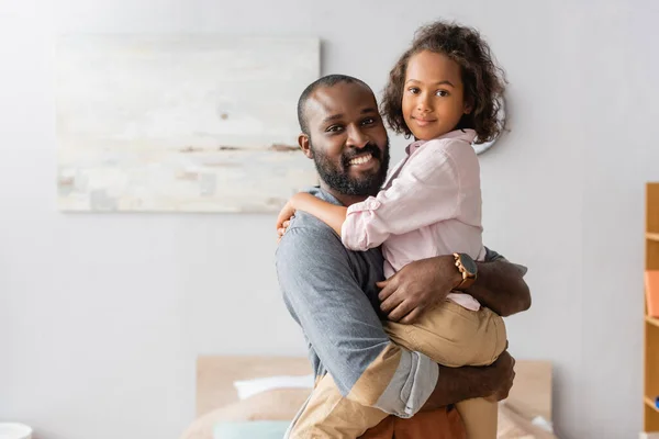 Jeune père afro-américain tenant l'enfant sur les mains tout en regardant la caméra ensemble — Photo de stock