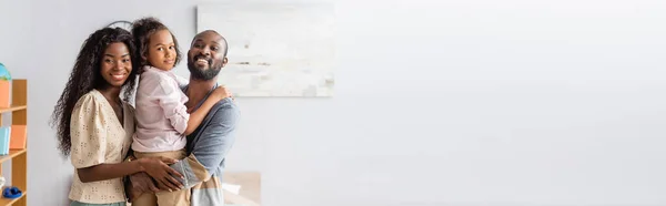 Website header of african american man holding daughter on hands while mother embracing them and looking at camera — Stock Photo