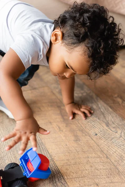 Foco seletivo da criança americana africana encaracolada brincando com caminhão de brinquedo no chão de madeira em casa — Fotografia de Stock