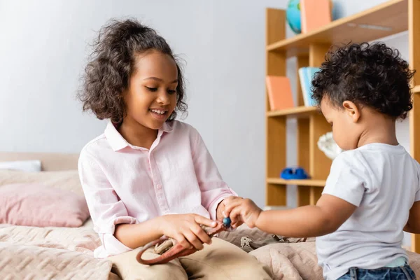 African american girl in white shirt sitting on bed and holding toy near brother — Stock Photo