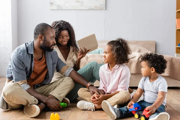 Famiglia afro-americana seduta al piano vicino a blocchi di costruzione e mamma tenendo libro — Foto stock