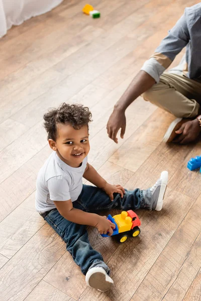 Vue recadrée de l'homme afro-américain près de son fils jouant avec camion jouet sur le sol — Photo de stock