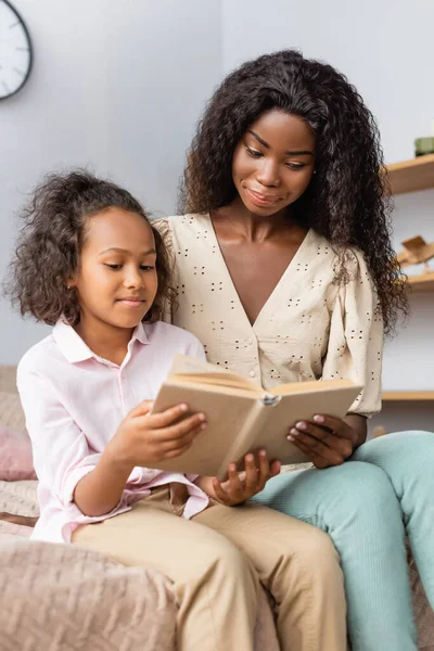 Afrikanisch-amerikanisches Kind liest Buch, während es bei der Mutter zu Hause sitzt — Stockfoto