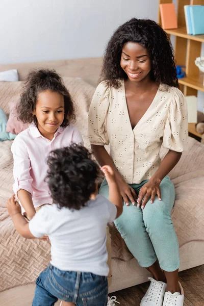 Високий кут зору афроамериканської жінки в повсякденному одязі біля дітей у спальні — стокове фото