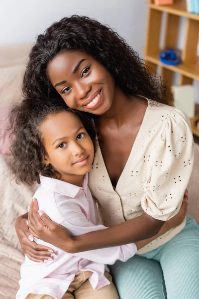 Afrikanisch-amerikanische Mutter und Kind schauen in die Kamera, während sie sich zu Hause umarmen — Stockfoto