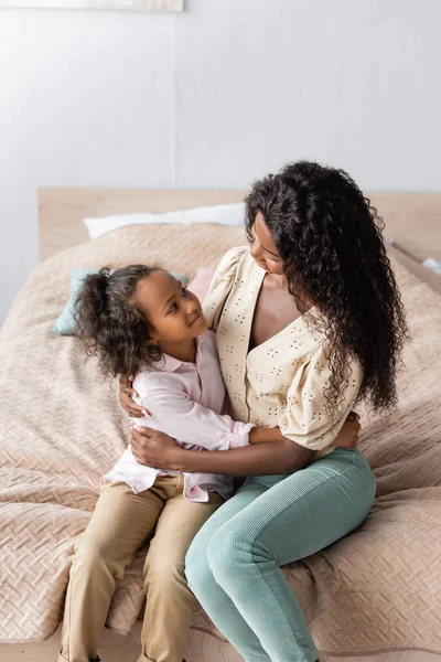 Aus der Vogelperspektive von afrikanisch-amerikanischen Mutter und Kind umarmen, während sie auf dem Bett sitzen — Stockfoto