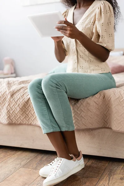 Vista cortada da mulher americana africana em blusa e calças usando tablet digital no quarto — Fotografia de Stock