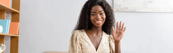 Horizontal image of african american woman waving hand while looking at camera — Stock Photo