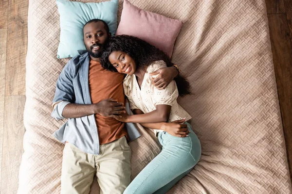 Vista dall'alto dell'uomo afro-americano che abbraccia la moglie mentre giace a letto in abiti casual — Foto stock