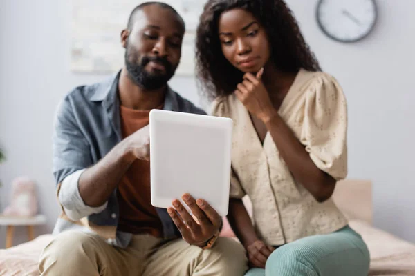 Selektiver Fokus eines afrikanisch-amerikanischen Mannes, der ein digitales Tablet in der Nähe seiner nachdenklichen Frau hält — Stockfoto