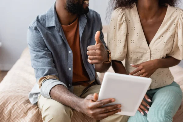 Ausgeschnittene Ansicht eines afrikanisch-amerikanischen Mannes, der ein digitales Tablet in der Hand hält und den Daumen in der Nähe seiner Frau zeigt — Stockfoto