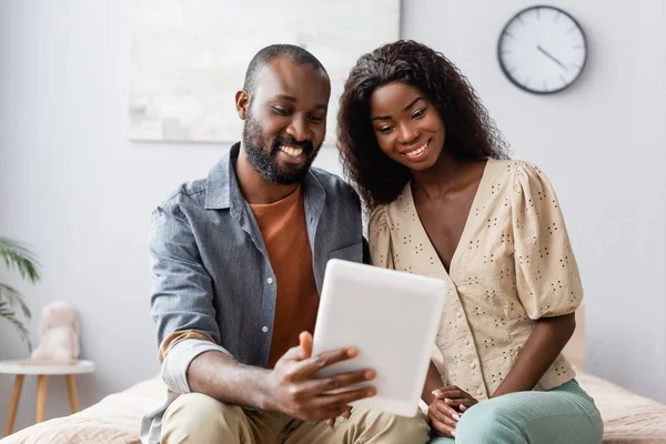 Молода подружня пара афроамериканців користується цифровим планшетом, сидячи у спальні. — стокове фото