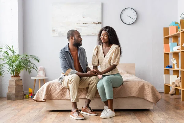 Jeune couple afro-américain en vêtements décontractés se tenant la main et se regardant dans la chambre — Photo de stock