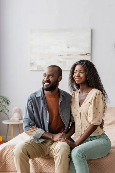 Jovem afro-americano marido e mulher em roupas casuais olhando para longe enquanto sentado na cama — Fotografia de Stock