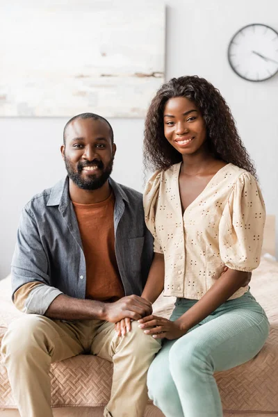 Молода афроамериканська пара у повсякденному одязі, яка дивиться на камеру, сидячи у спальні. — стокове фото