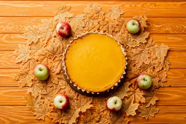 Top view of thanksgiving pumpkin pie with apples and autumnal foliage on wooden background — Stock Photo