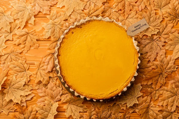 Top view of thanksgiving pumpkin pie with autumnal foliage on wooden background — Stock Photo