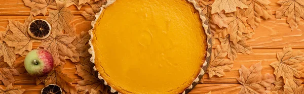 Vista dall'alto torta di zucca con mele, agrumi secchi e fogliame autunnale su fondo di legno, colpo panoramico — Foto stock