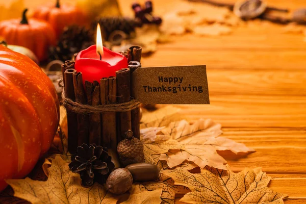Selective focus of burning candle with happy thanksgiving card and autumnal decoration on wooden background — Stock Photo