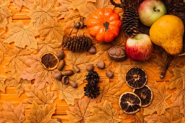 Vista dall'alto della decorazione autunnale e cibo sparso da cesto di vimini su fogliame dorato su sfondo di legno — Foto stock