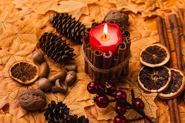 Brennende Kerze mit herbstlicher brauner Dekoration auf goldenem Laub — Stockfoto