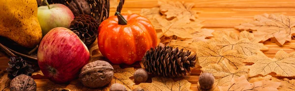 Decorazione autunnale e cibo sparso da cesto di vimini su fogliame dorato su sfondo di legno, colpo panoramico — Foto stock