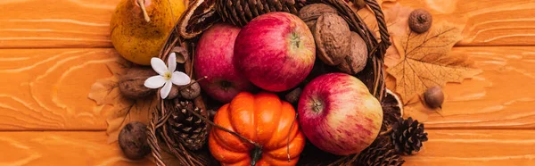Top view of wicker basket with autumnal harvest on wooden background, panoramic shot — Stock Photo