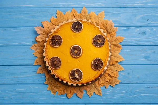 Vue de dessus de tarte à la citrouille décorée avec feuillage doré sur fond de bois bleu — Photo de stock