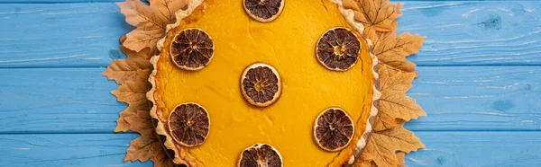 Draufsicht auf dekorierten Kürbiskuchen mit goldenem Laub auf blauem Holzhintergrund, Panoramaaufnahme — Stockfoto