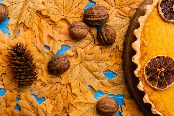 Top view of pumpkin pie on autumnal foliage with walnuts and cone — Stock Photo