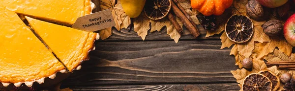 Top view of autumnal decoration and pumpkin pie with happy thanksgiving card on brown wooden background, panoramic shot — Stock Photo