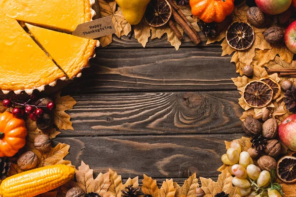 Vista superior de la decoración otoñal y pastel de calabaza con feliz tarjeta de acción de gracias sobre fondo de madera marrón - foto de stock