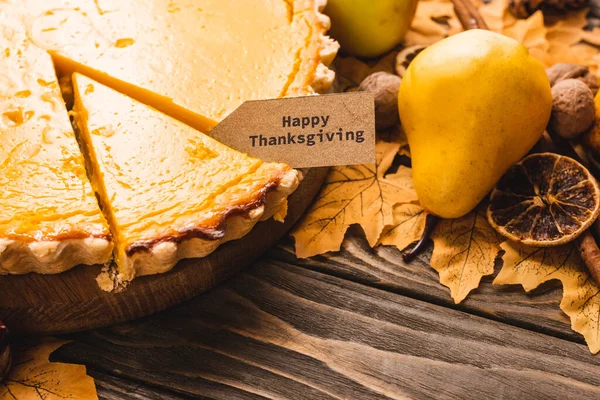 Close up view of autumnal decoration and pumpkin pie with happy thanksgiving card on brown wooden background — Stock Photo
