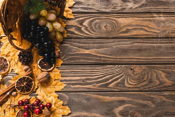 Top view of autumnal harvest scattered from basket on foliage on brown wooden background — Stock Photo