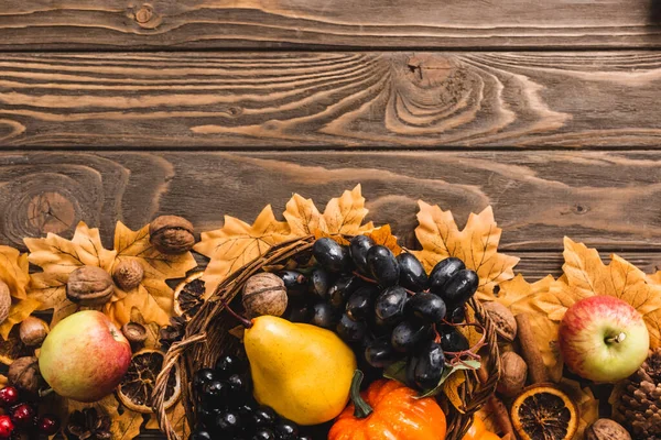 Top view of autumnal harvest in basket on foliage on brown wooden background — Stock Photo