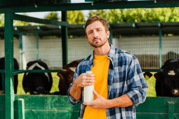 Rancher in checkered shirt holding bottle of fresh milk while looking at camera near cowshed — Stock Photo