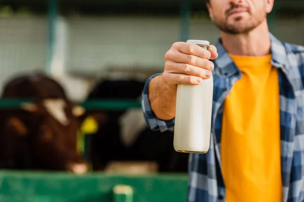 Vue recadrée du rancher en chemise à carreaux montrant une bouteille de lait frais, mise au point sélective — Photo de stock