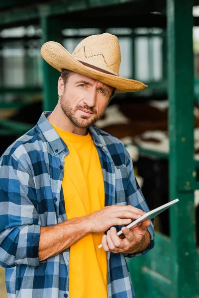 Rancher in straw hat and checkered shirt using digital tablet while looking at camera — Stock Photo