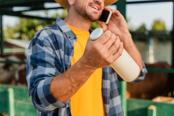 Partial view of farmer in plaid shirt talking on mobile phone and holding bottle of fresh milk, selective focus — Stock Photo