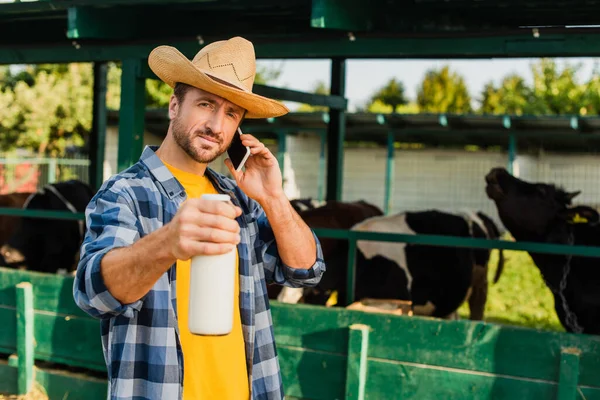 Bauer in kariertem Hemd und Strohhut hält beim Telefonieren eine Flasche Milch in der Hand — Stockfoto