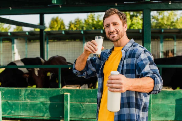 Selektiver Fokus des Bauern im karierten Hemd mit Glas und Flasche frischer Milch in der Nähe des Kuhstalls — Stockfoto