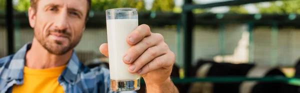 Horizontal concept of farmer showing glass of fresh milk while looking at camera — Stock Photo