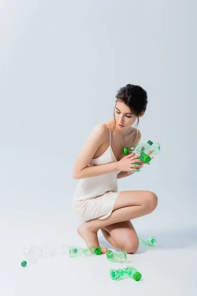 Брюнетка в шовковій сукні тримає пластикові пляшки на білому, концепція екології — стокове фото